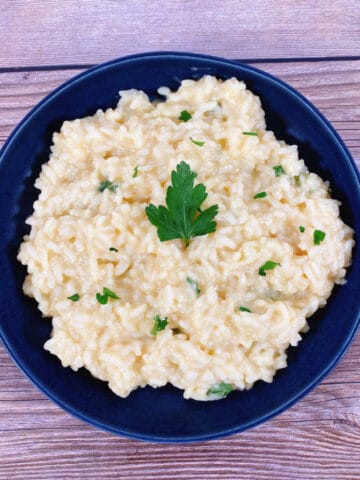 creamy parmesan risotto sprinkled with fresh parsley sits in a navy blue bowl on a wooden background