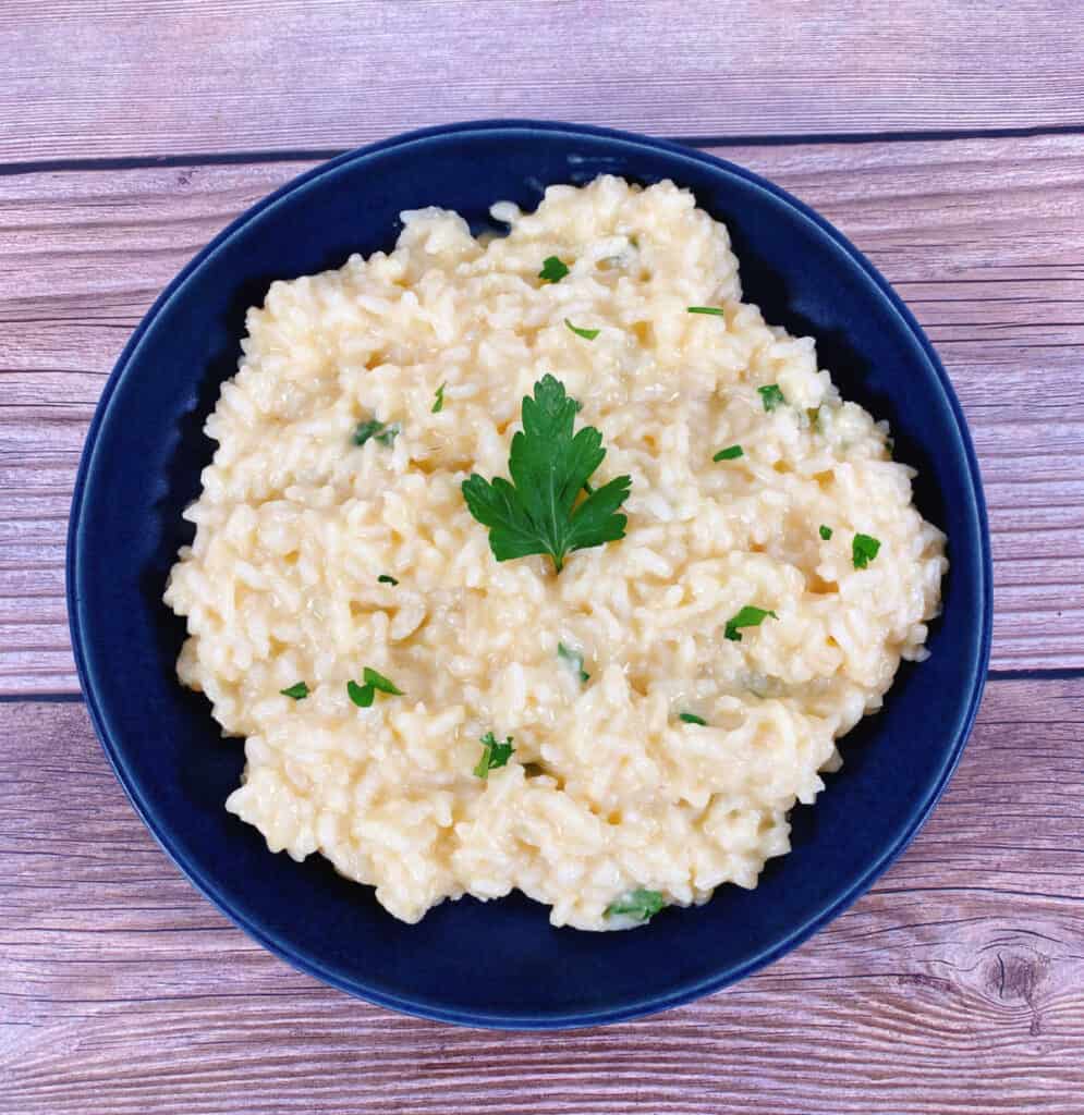 creamy parmesan risotto sprinkled with fresh parsley sits in a navy blue bowl on a wooden background