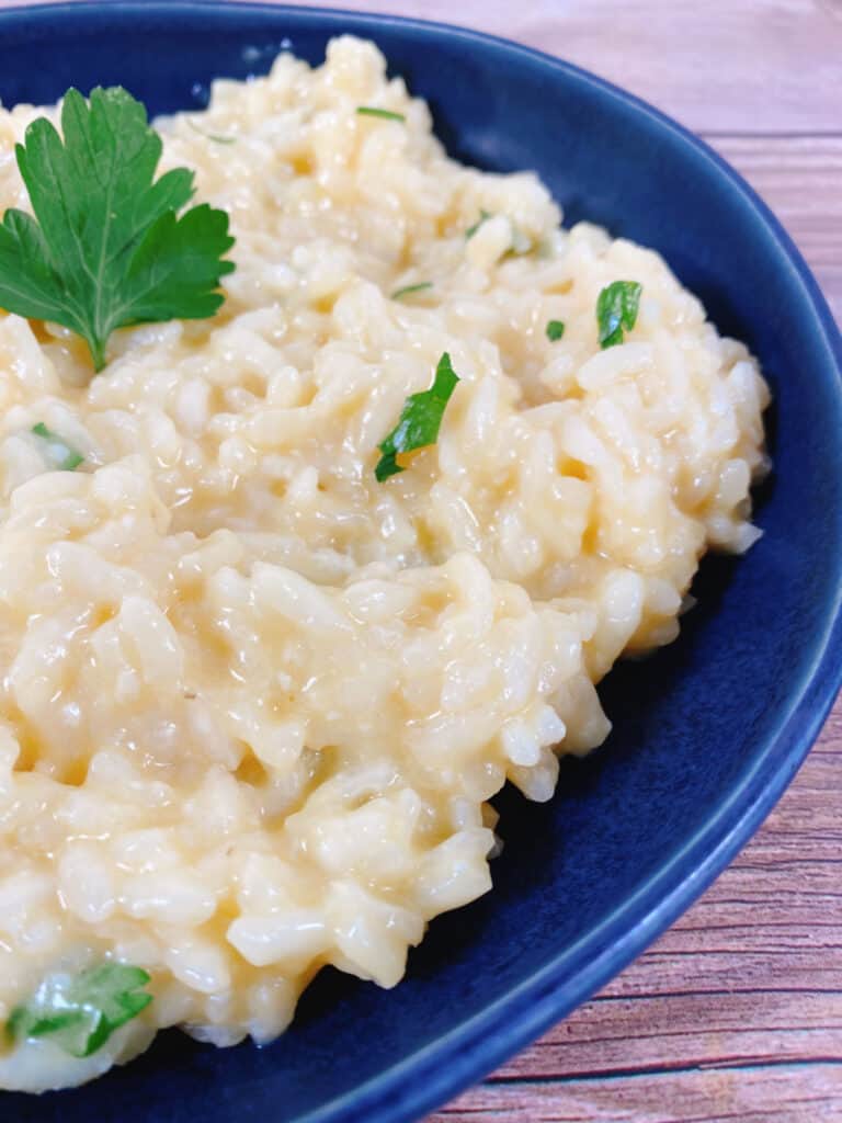 creamy parmesan risotto sits in a navy blue bowl on a wooden background