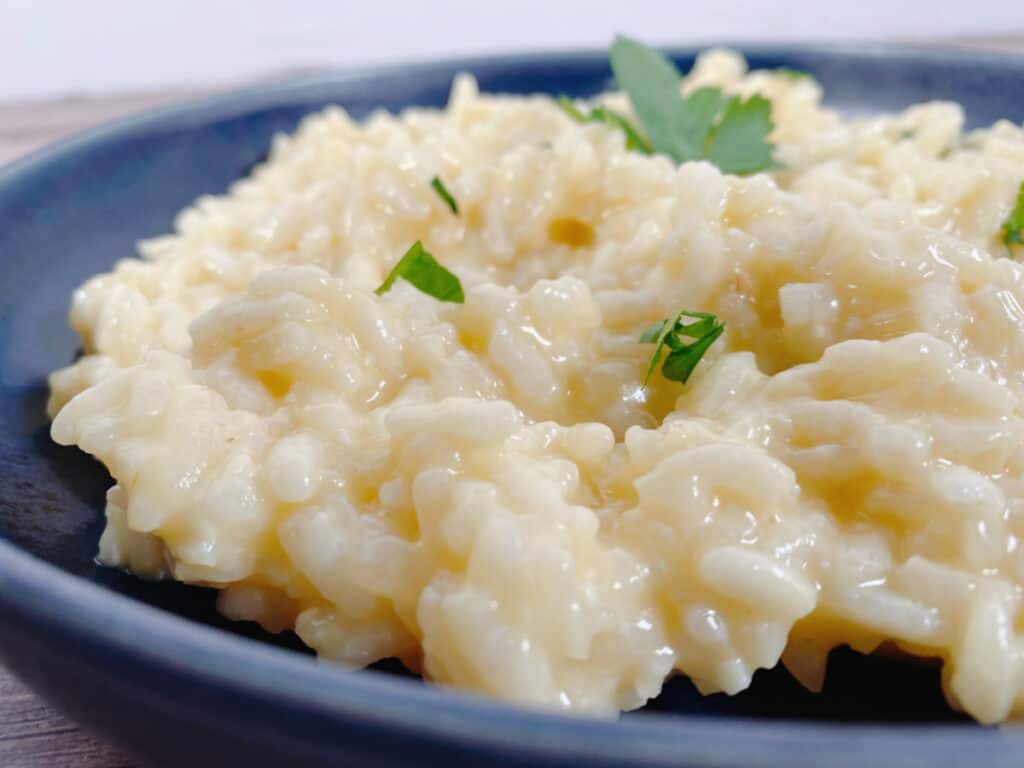 creamy parmesan risotto sprinkled with fresh parsley sits in a navy blue bowl on a wooden background