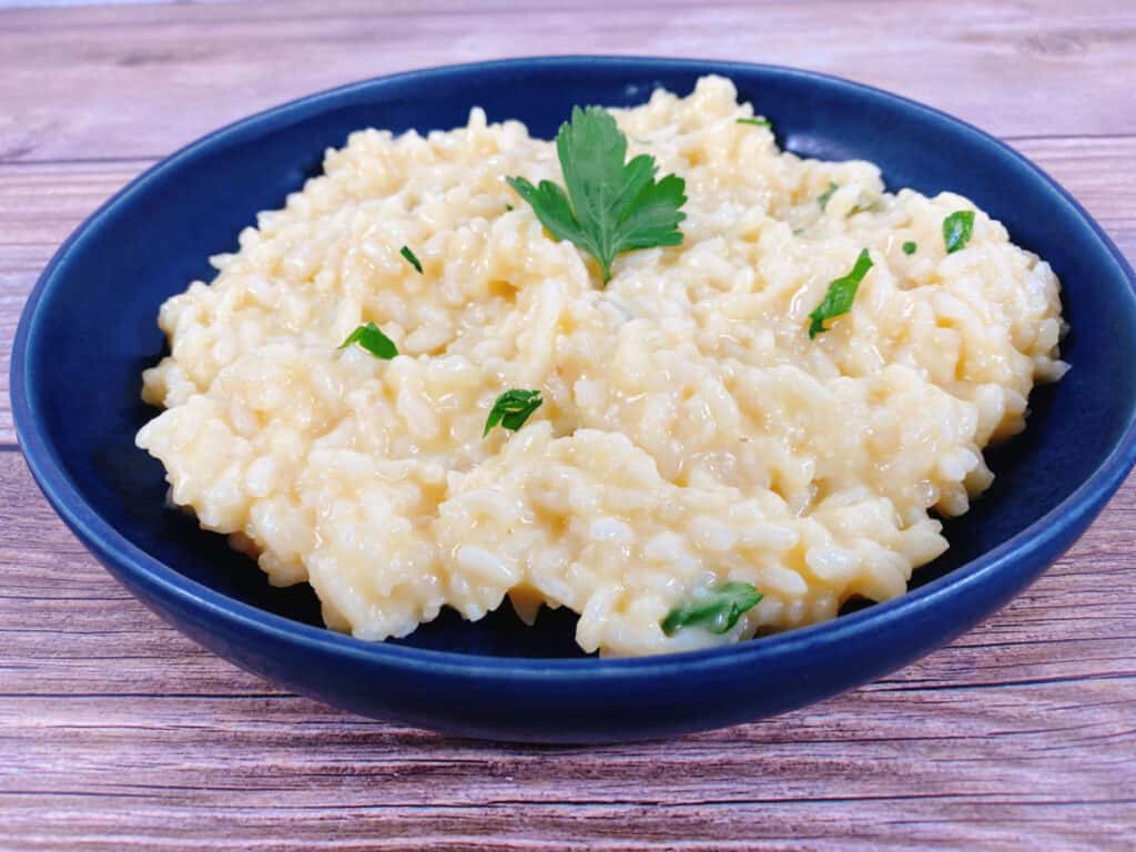 creamy parmesan risotto sprinkled with fresh chopped parsley sits in a blue bowl on a wooden background