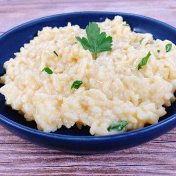 creamy parmesan risotto sprinkled with fresh chopped parsley sits in a blue bowl on a wooden background