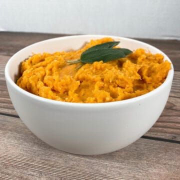 mashed sweet potatoes in a white bowl, topped with fresh sage leaves