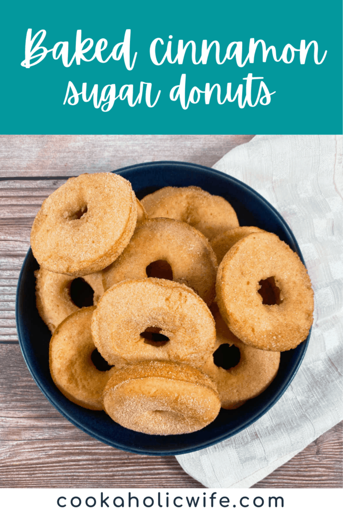 on a wooden background sits a navy blue bowl stacked high with baked cinnamon sugar donuts 