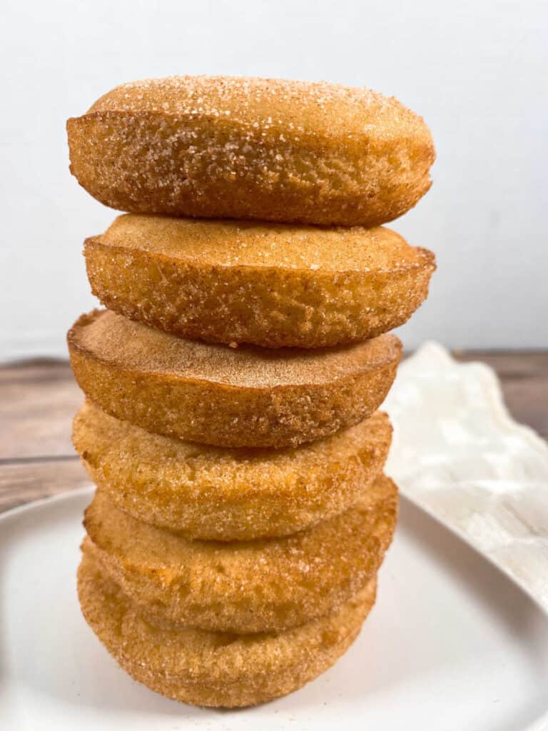 a tower of 6 cinnamon sugar baked donuts are stacked on top of each other, sitting on a white plate with a cream napkin folded in the background