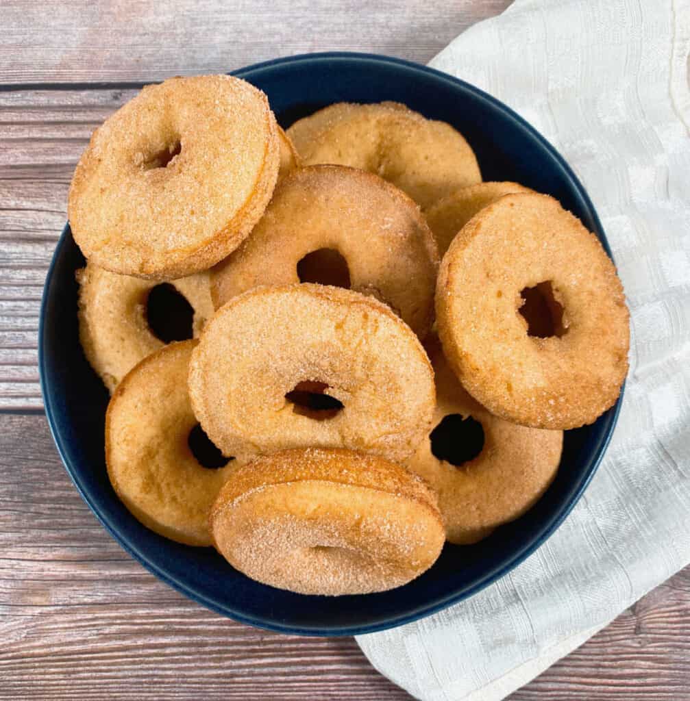 in a shallow navy blue bowl on a wooden background sits a pile of cinnamon sugar baked donuts