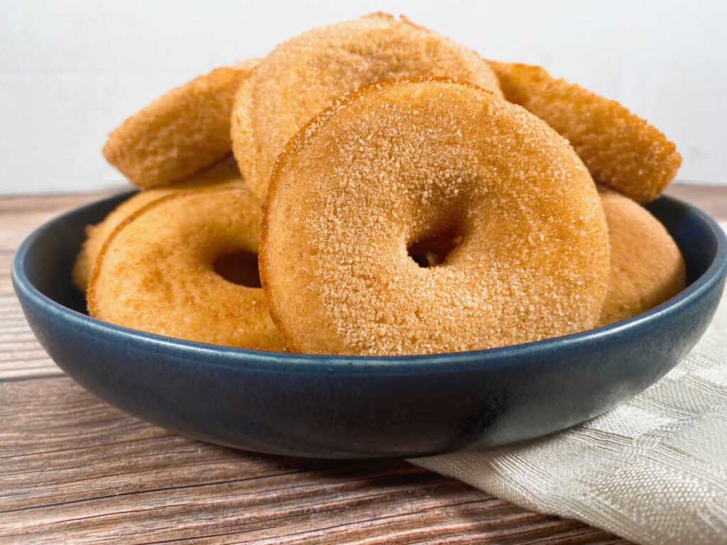 forward facing view of baked cinnamon sugar donuts sitting in a navy blue bowl on a wooden background