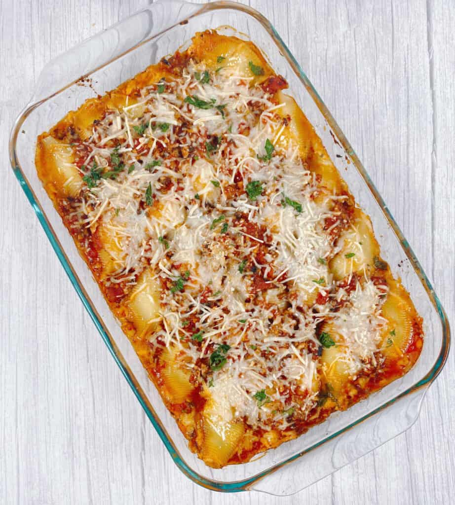 9x13 dish of baked cheesy vegetarian stuffed shells on a white wooden background. Dish is topped with cheese and fresh parsley 