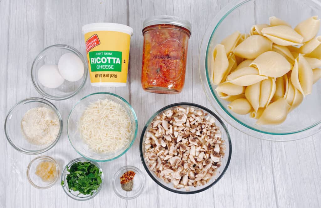 Ingredients for Cheesy Vegetarian Stuffed Shells - eggs, ricotta cheese, spaghetti sauce, jumbo shells, parmesan cheese, shredded mozzarella cheese, chopped mushrooms, garlic, parsley, crushed red pepper, salt and pepper.