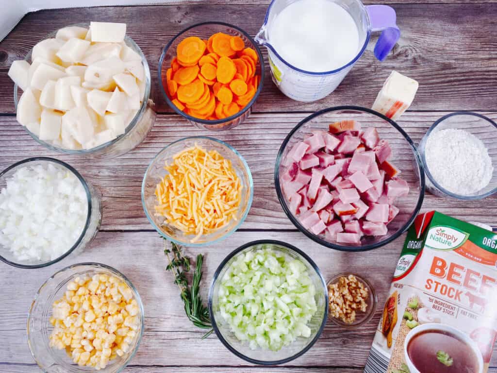 Ingredients for creamy ham and potato soup. Ingredients are potatoes, carrots, celery, onion, corn, ham, cheese, milk, butter, flour, beefr broth, garlic, rosemary and thyme. 