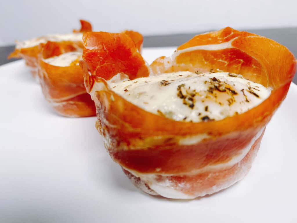 Crispy prosciutto wraps around an oven-baked egg cup, topped with mozzarella cheese and italian seasoning. 