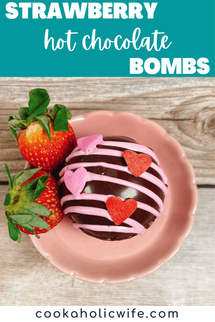 Close up image of a strawberry hot chocolate bomb sitting on a small pink stand with fresh strawberries. 