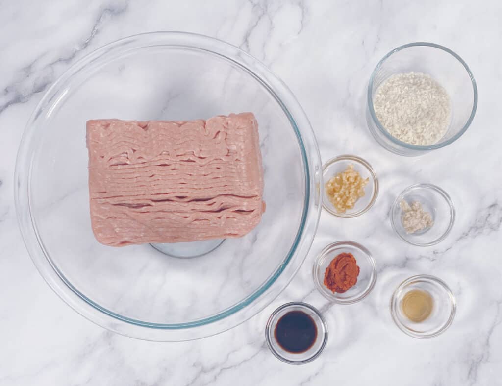 Ingredients for the Thai Turkey Burgers sit in glass bowls on a marble background. Ingredients are ground turkey, soy sauce, garlic, ginger, fish sauce, thai red curry paste and panko breadcrumbs. 