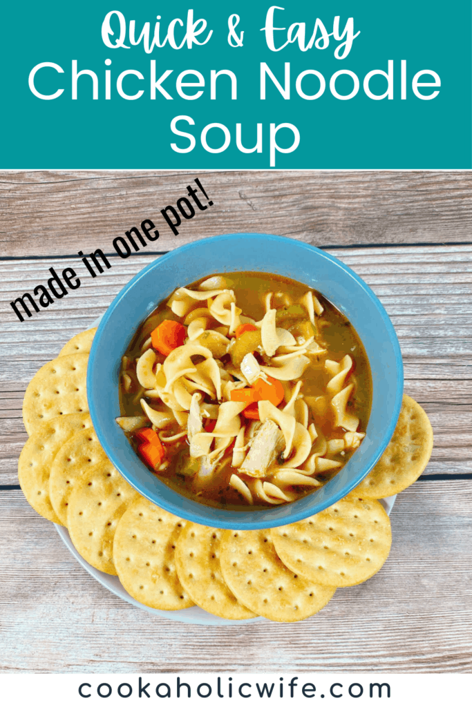 on a wooden background sits a blue bowl surrounded by round crackers. The bowl is full of chicken noodle soup.