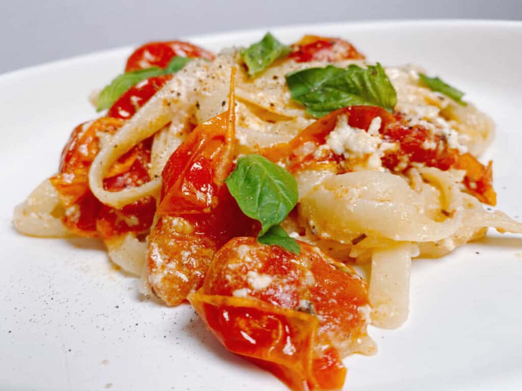 close up of baked feta tomato fettuccine on a white plate, topped with fresh basil. 