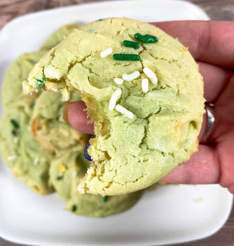 cake mix cookie with a bite missing is held up above the plate of stacked cookies. 