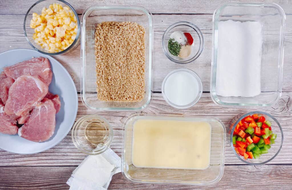 Ingredients for indiana pork tenderloin sandwich sit on a wooden background. Sliced and pounded thin pork loin, panko bread crumbs, Wondra flour, egg, corn, bell pepper, milk, vinegar, cream cheese and seasonings. 