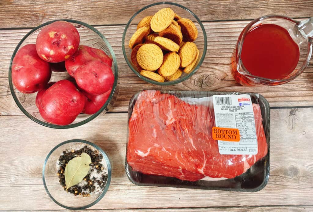 Ingredients for sour beef and dumplings sit on a wooden background. Potatoes, gingersnap cookies, red wine vinegar, spices and beef roast. Not pictured, carrots and onions, 