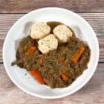 Baltimore's take on Sauerbrauten, a bowl of sour beef and dumplings sits on a wooden background. The gravy is made from gingersnap cookies