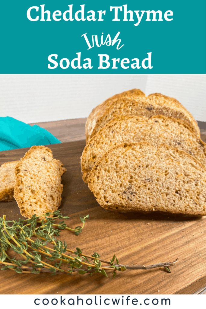 slices of cheddar thyme irish soda bread slt on a dark wooden cutting board. fresh thyme sits off to the side. 