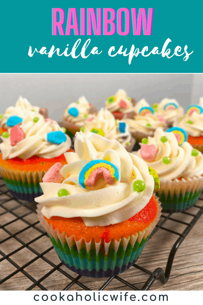 Image for Pinterest. Text overlay on top of teal background at top reads Rainbow Vanilla Cupcakes in a mixture of block and script font. Below that is the image of rainbow colored cupcakes with vanilla frosting sitting on a wire cooling rack. At the bottom of the image is black text over a white background, reading www.cookaholicwife.com