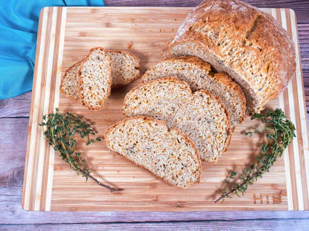 slices of cheddar thyme irish soda bread are arranged on a wooden cutting board. fresh thyme sits around the slices. A teal napkin sits off in the background. 