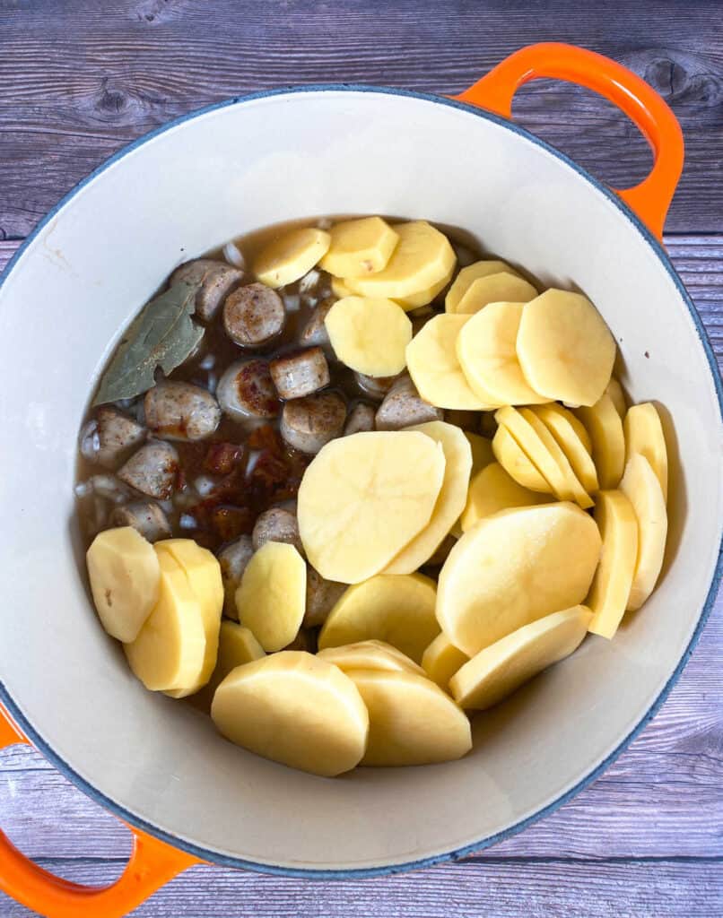 Image before simmering and baking the coddle. A dutch oven has the bacon, sausages, onions and potatoes layered in ready for cooking. 