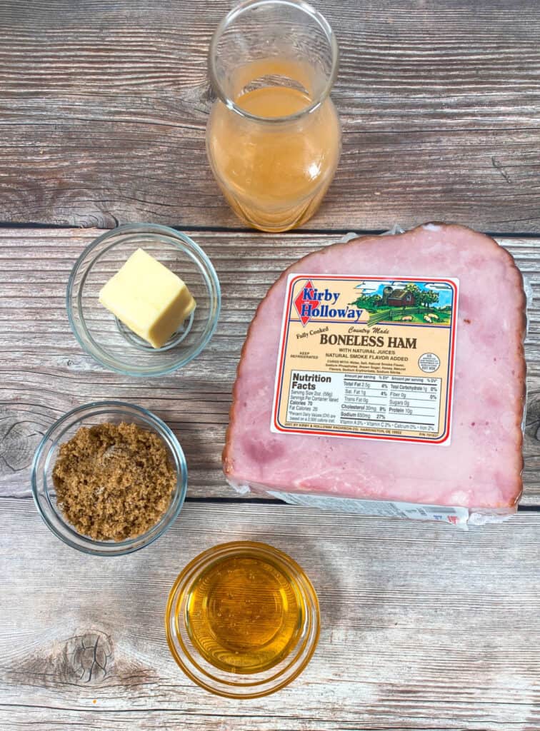 ingredients for honey bourbon baked ham sit on a wooden background. A ¼ ham, brown sugar, honey, butter and bourbon make up the glaze. 