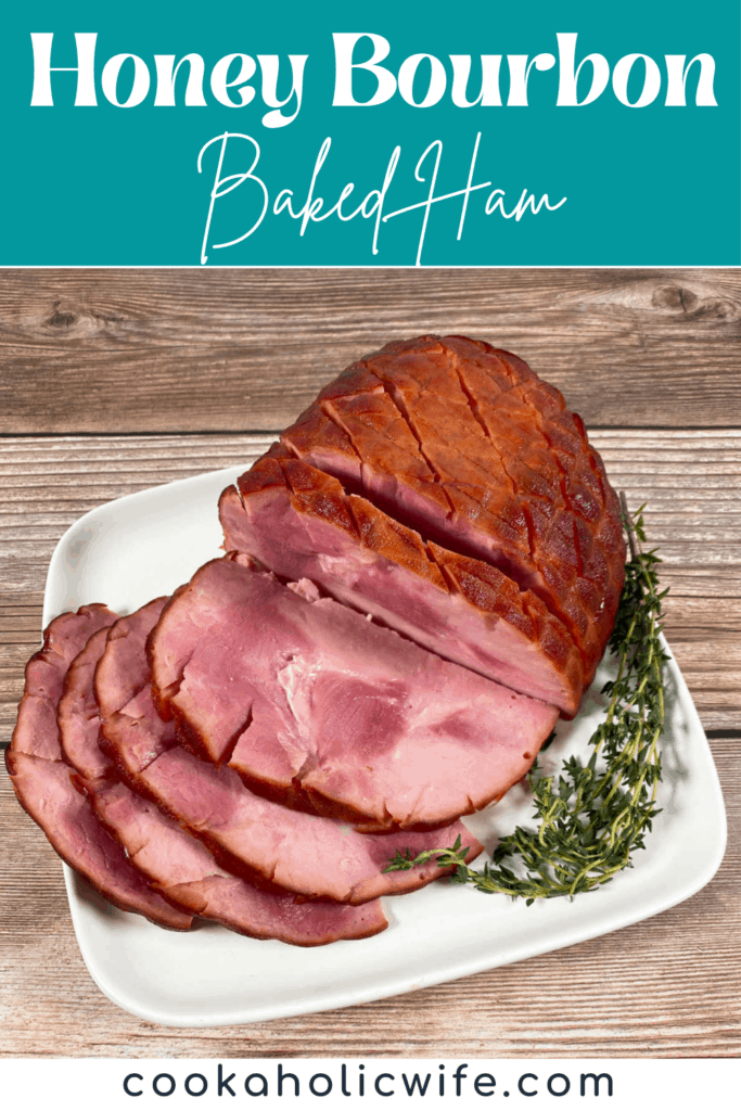 A partially sliced ham sits on a white plate on a wooden background. Next to the ham is fresh thyme. The ham is covered in a sweet glaze made with bourbon, brown sugar, honey and butter. 