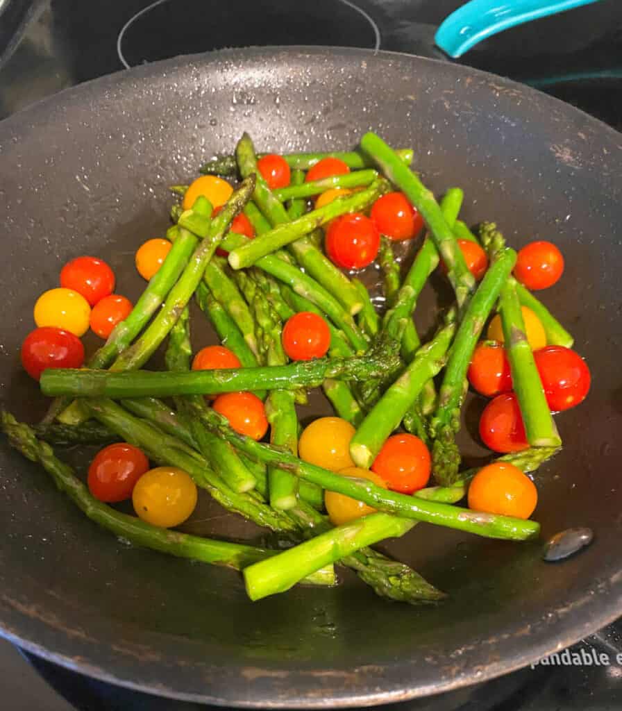 Prep image of the asparagus bacon caprese salad. The asparagus and tomatoes are cooking in a saucepan. 