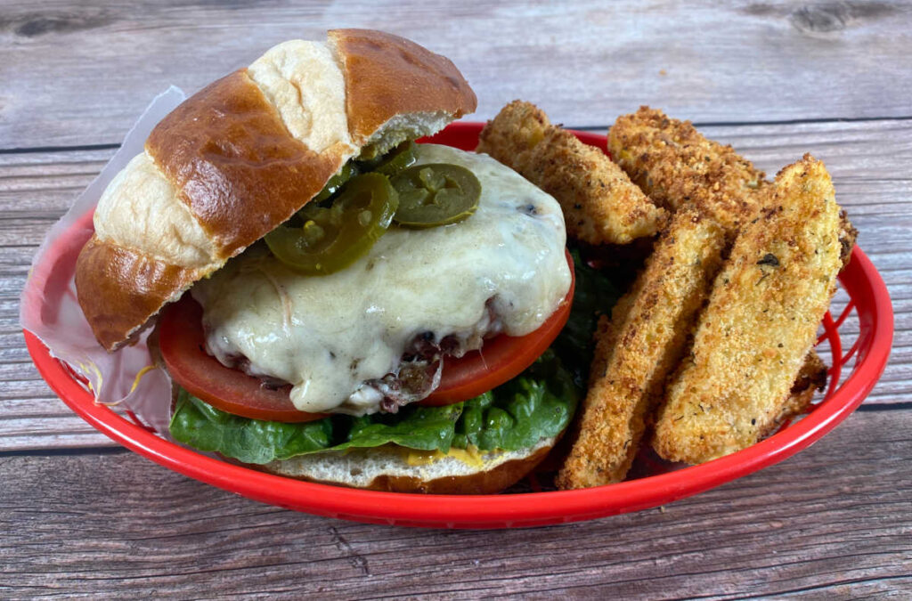 close up of burger in a red basket. Top pretzel roll is tilted off the burger to show the toppings and cheese on the burger.