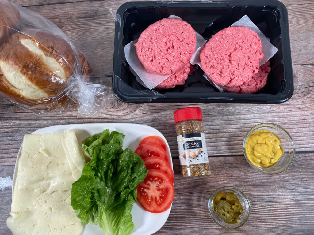 ingredients for the burger; burger patties, pretzel rolls, Havarti cheese, lettuce, tomato slices, grilling seasoning, jalapeno mustard and pickled jalapenos. 