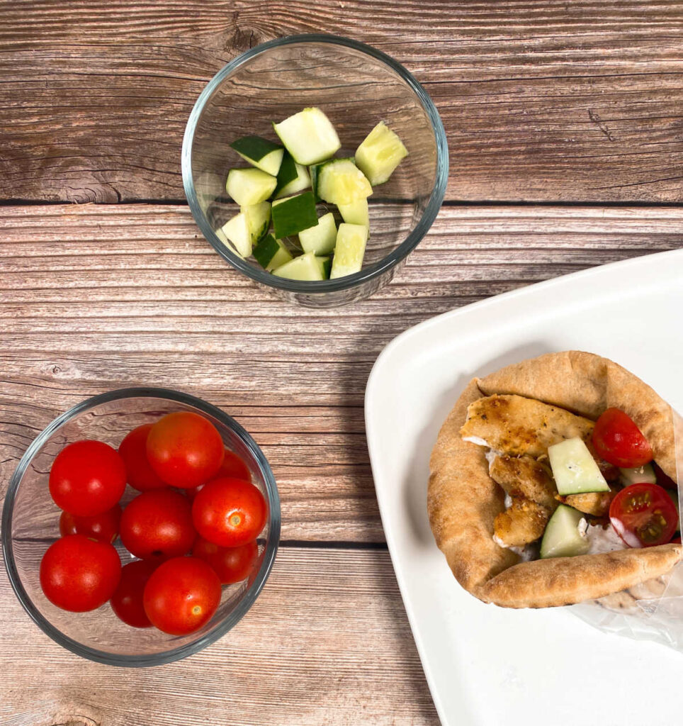 overhead image of open end of the gyro on a white plate. Cucumber and tomato are in bowls next to the plate.