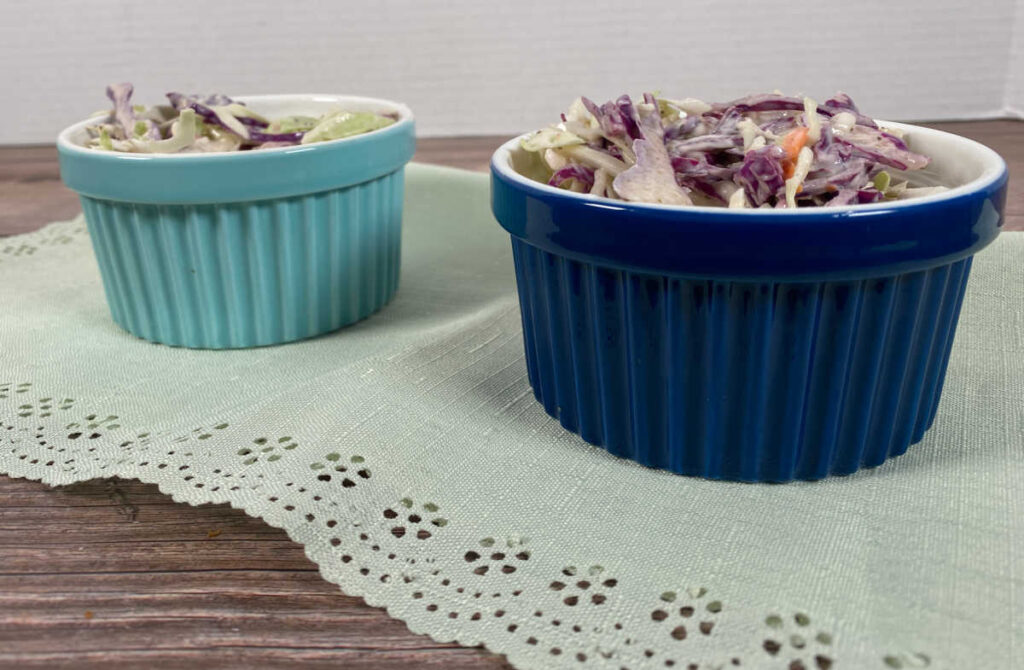 Prepared coleslaw sits in a turquoise and navy blue ramekin on a light green napkin.