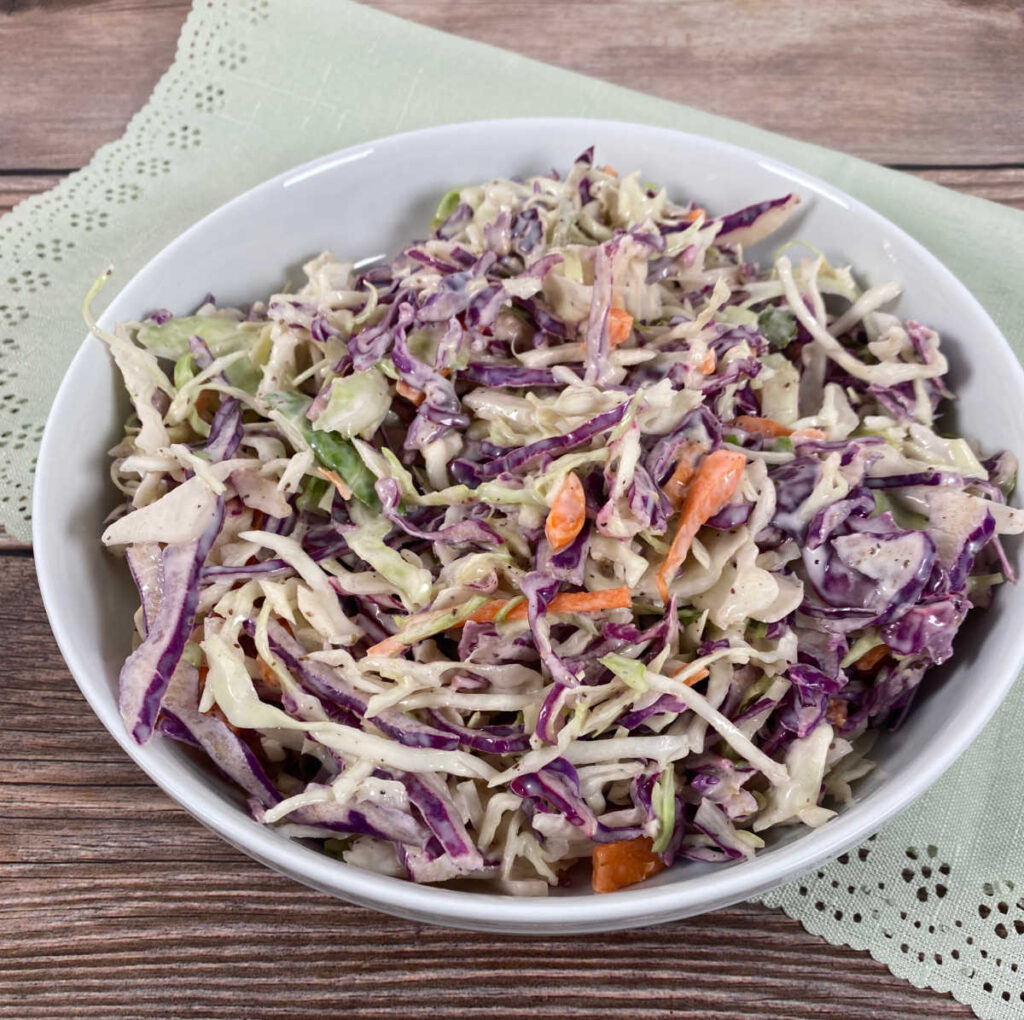 A shallow bowl of coleslaw, made with coleslaw mix and red cabbage sits on a wooden background.