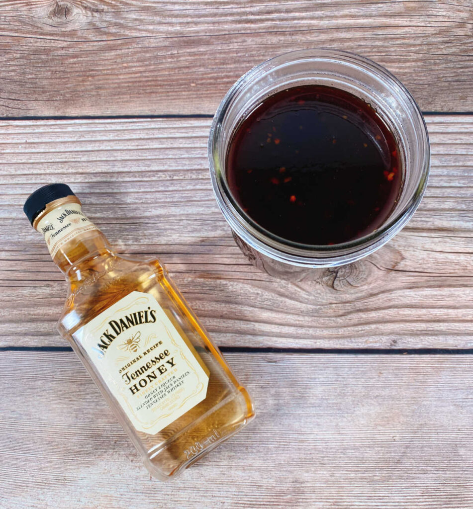 homemade honey whiskey bbq sauce sits in a mason jar with a bottle of jack daniels honey whiskey next to it 