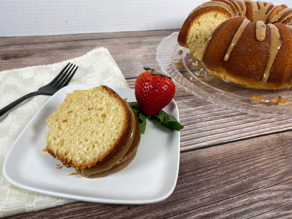 slice of hot milk cake sits on a white plate, framed with a strawberry. The rest of the cake is in the background with the slice missing 