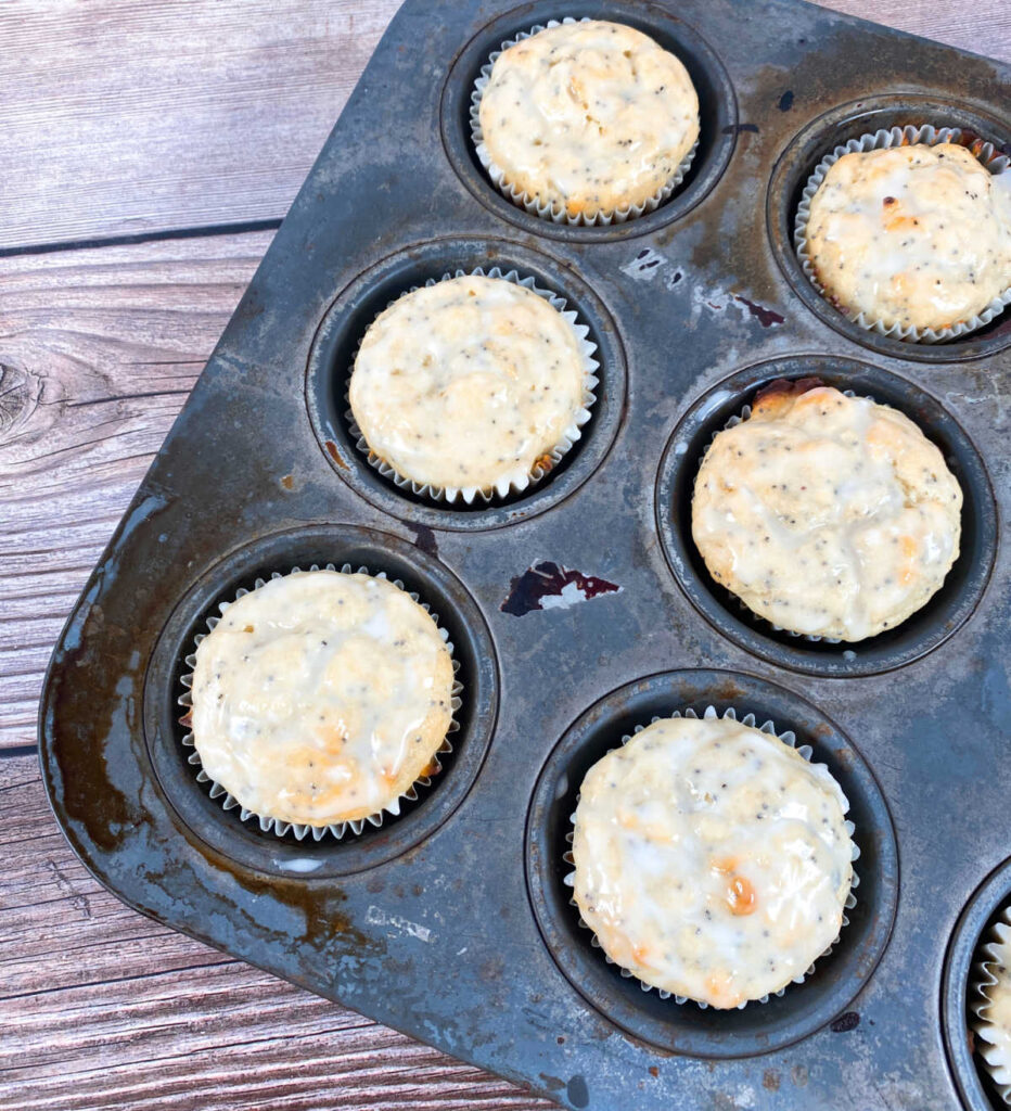 glazed lemon poppy seed muffins sit in a metal muffin pan. 