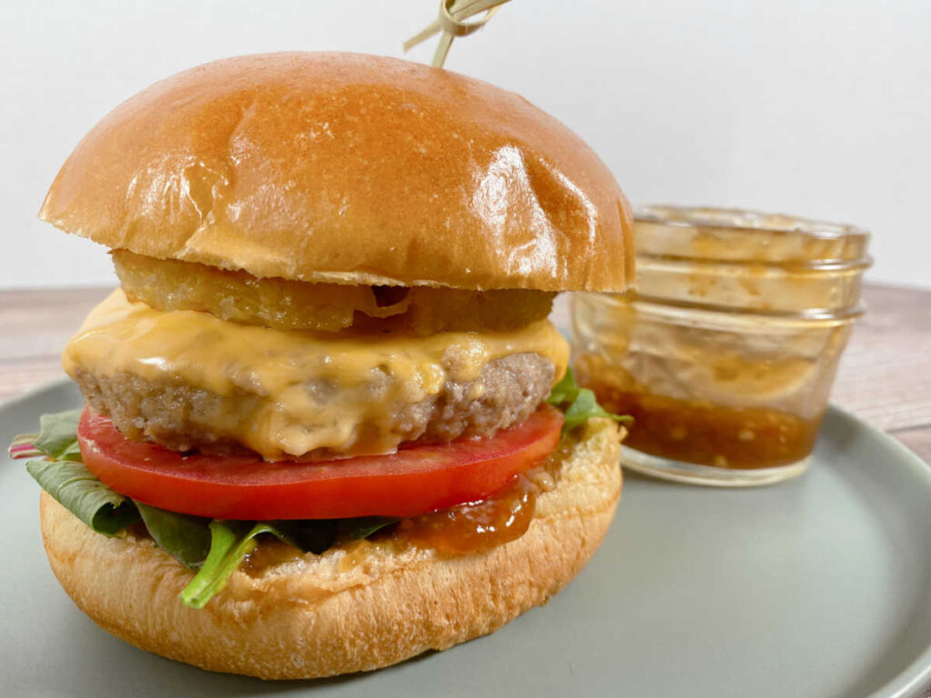 burger sitting on a light green plate. In the background is a small mason jar of the teriyaki sauce.