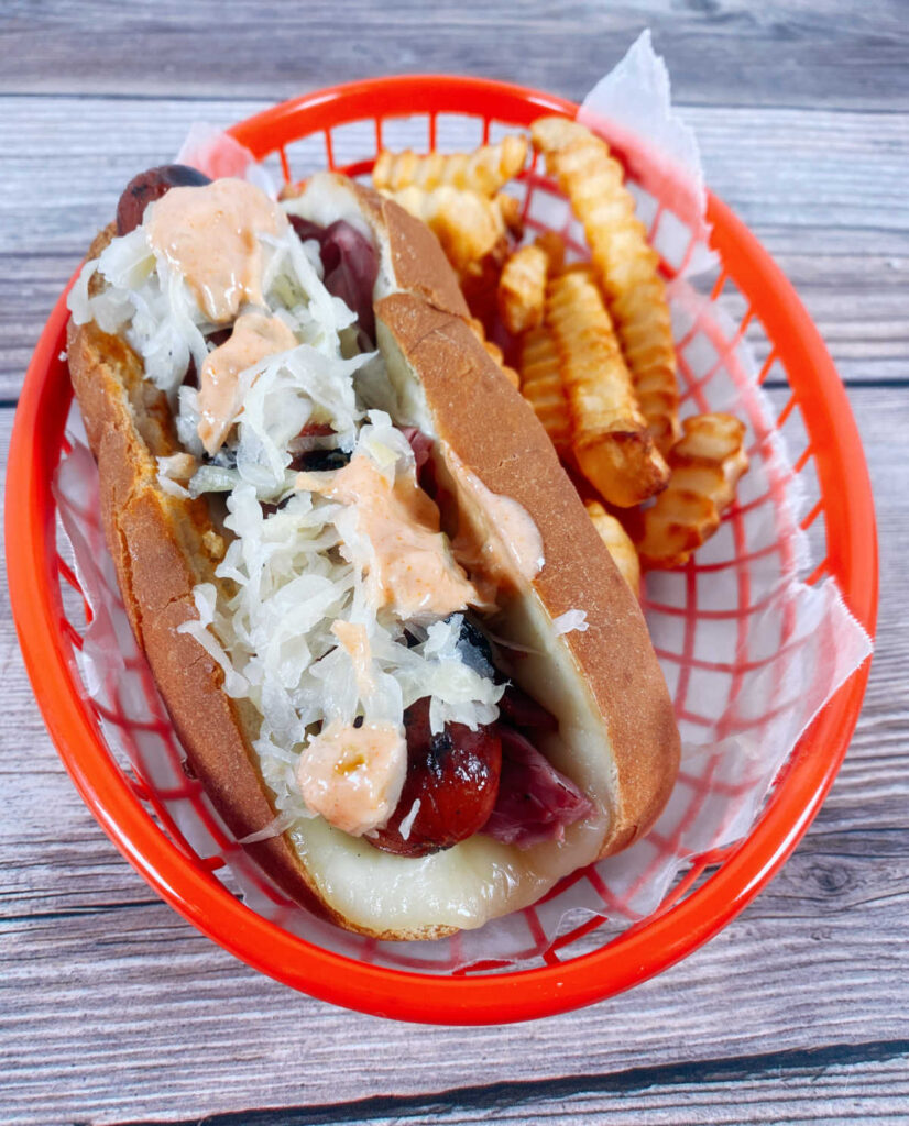 Hot dog sits in a red tray, covered in toppings with fries off to the side. 