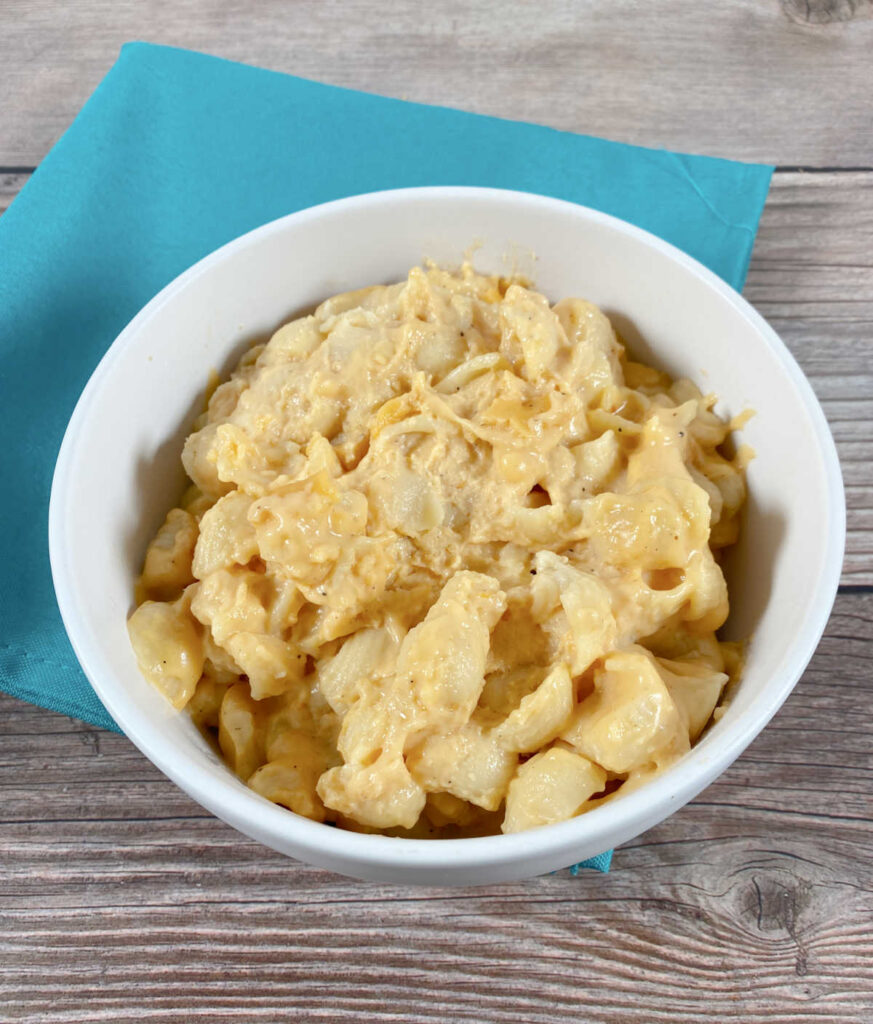 large white bowl of macaroni and cheese sits on a wooden background. 