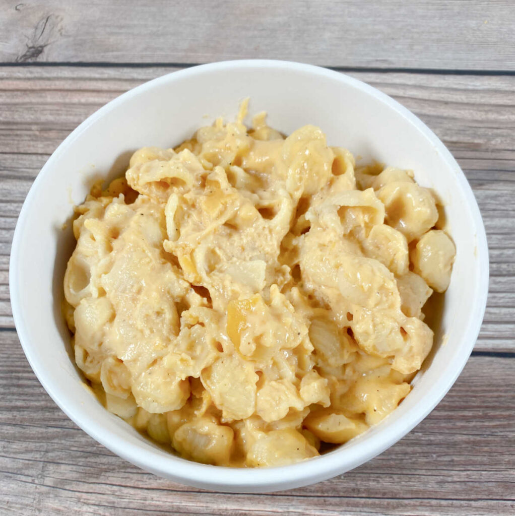 white bowl full of macaroni and cheese sits on a wooden background