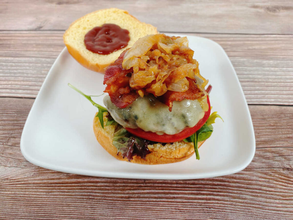 Burger, piled high with caramelized onions sits open faced on a white plate.
