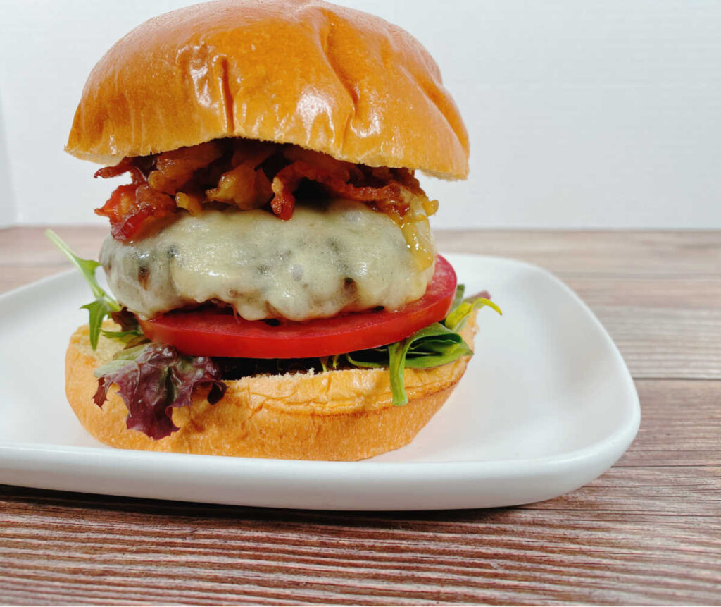 Assembled burger sits on a square white plate on a dark wooden background 