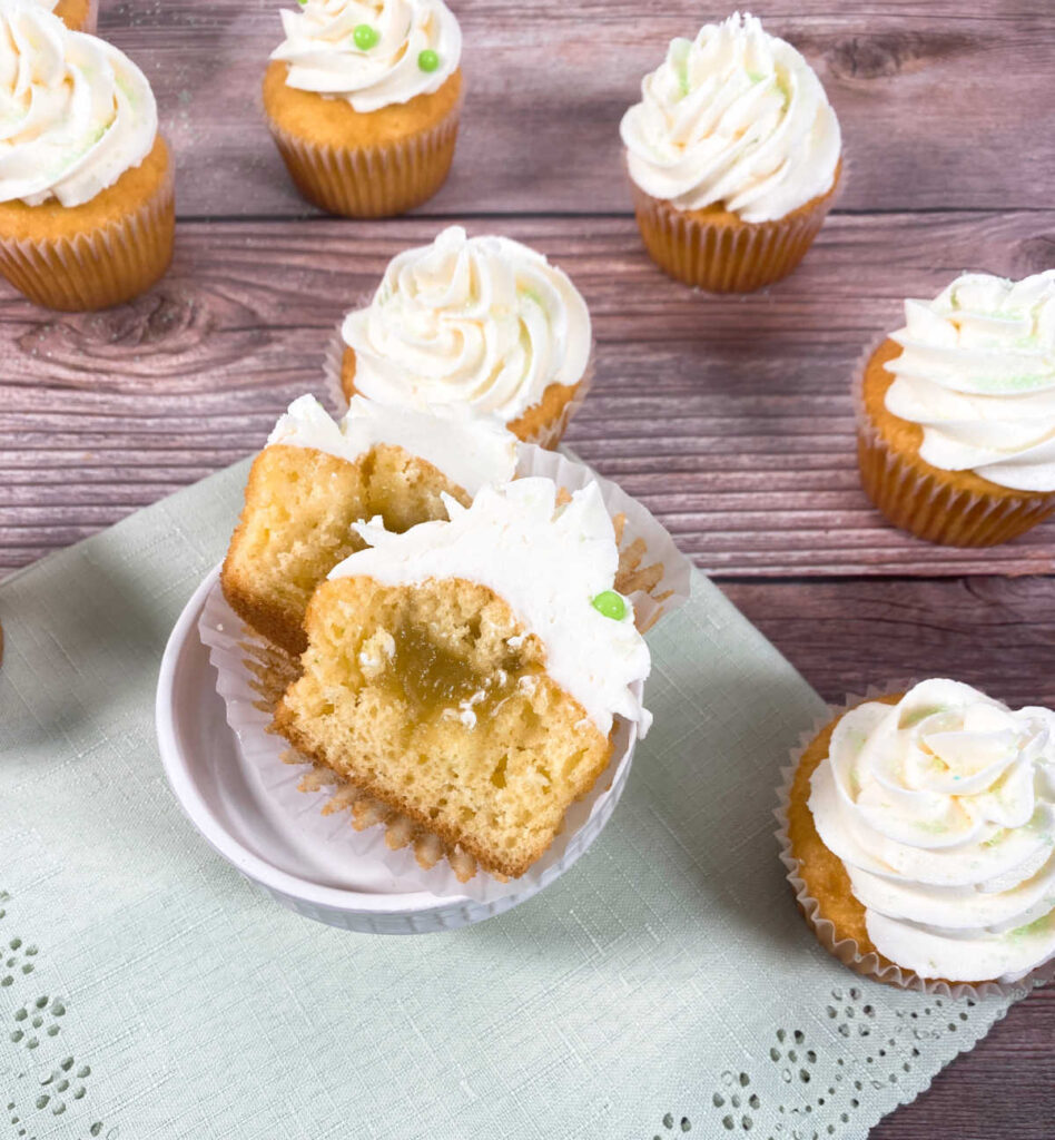 cupcake cut in half to show lime curd filling sits on a light green napkin. other decorated cupcakes surround it. 