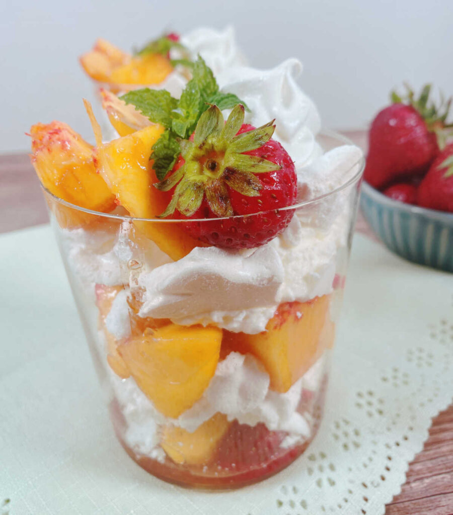 close up image of eton mess in a glass, topped with strawberries and peaches. 