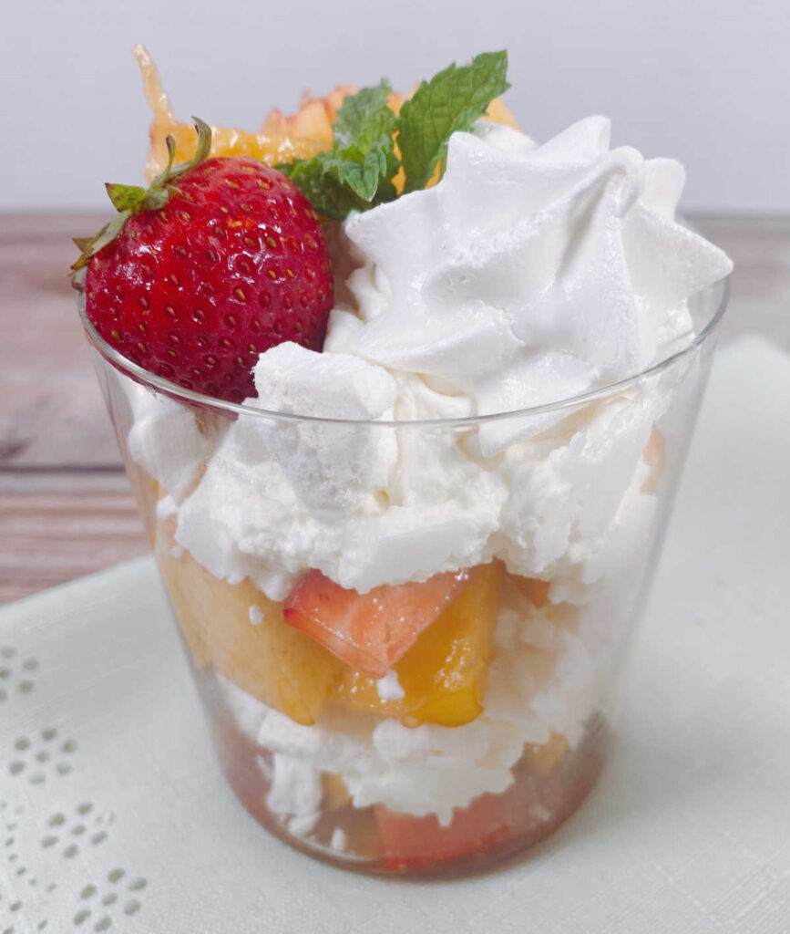 glass of layered eton mess sits on a light green napkin