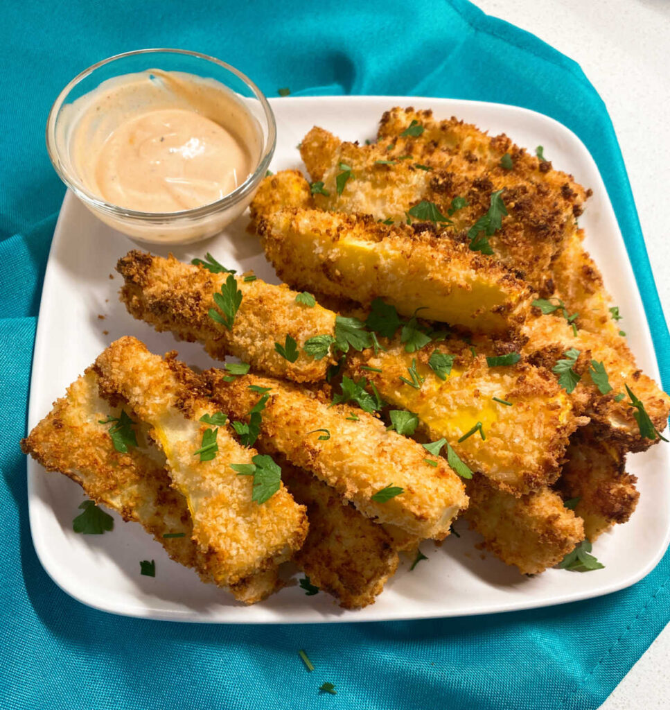 squash fries sit on a square white plate on a teal napkin. fries are garnished with parsley