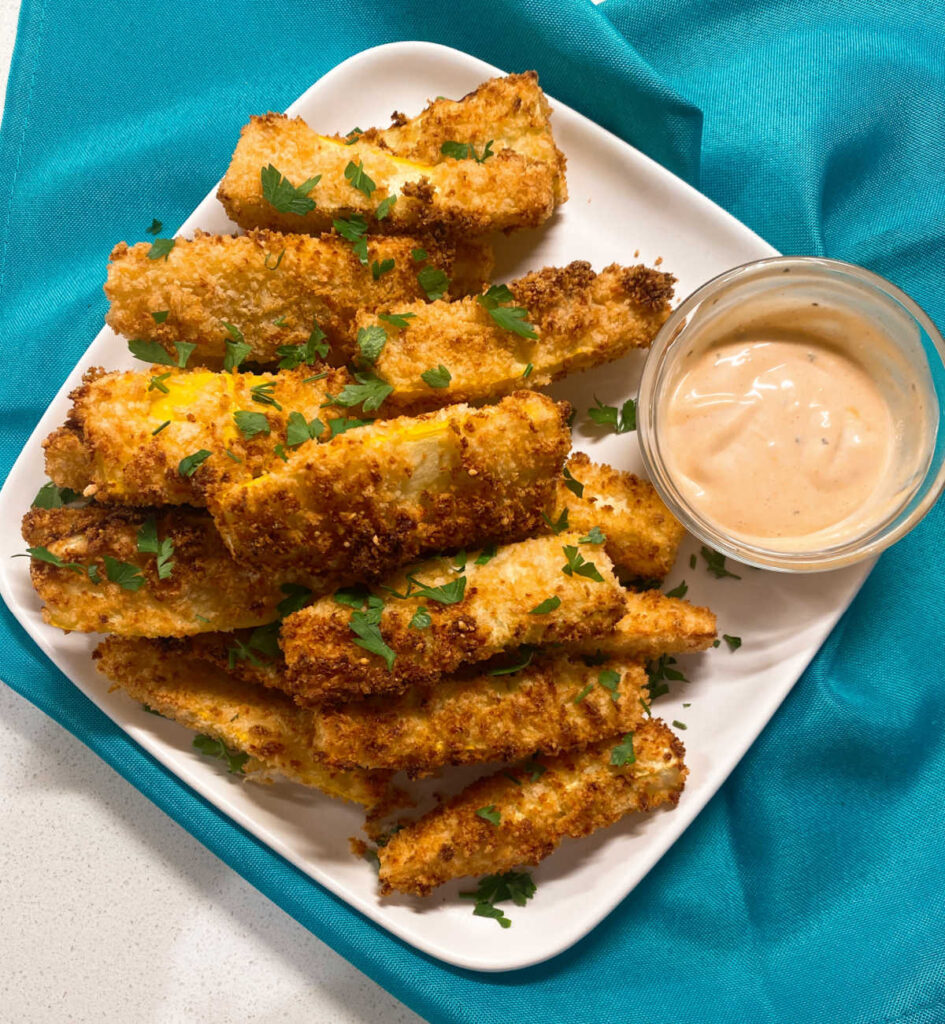 cripsy air fried squash wedges sit on a white plate, garnished with parsley on a teal napkin.