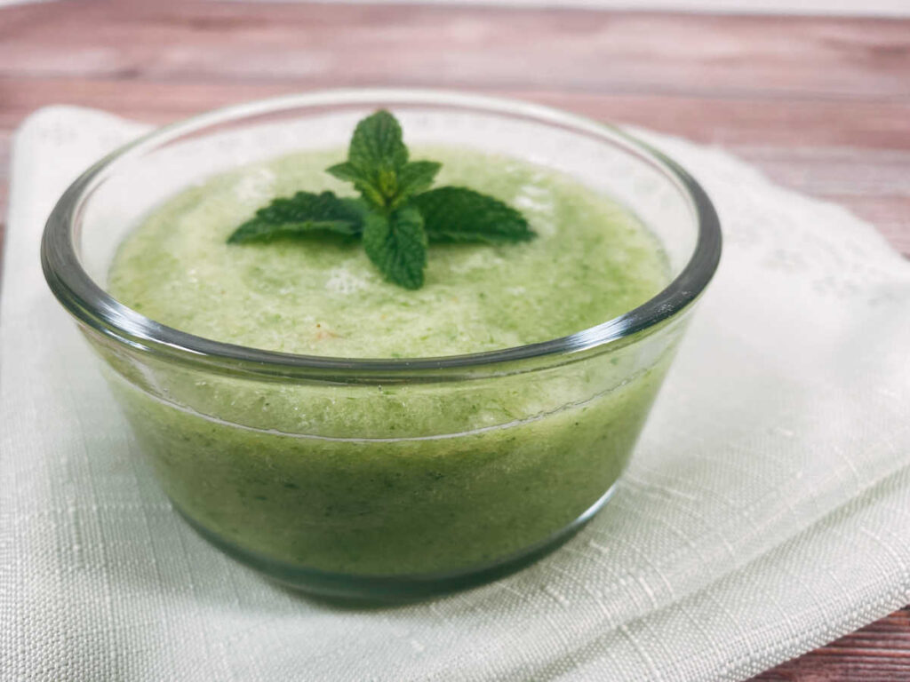 close up image of soup in a glass bowl on a light green scalloped napkin.